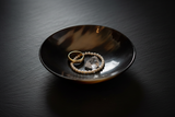 Haitian black horn bowl holding gold ring and pearl bracelet on dark slate surface with moody lighting
