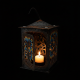 Haitian hand-painted metal lantern on a black background with candle glowing inside illuminating the colorful cut-out floral patterns