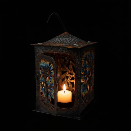 Haitian hand-painted metal lantern on a black background with candle glowing inside illuminating the colorful cut-out floral patterns