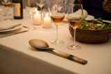 Haitian all-horn salad spoon on luxury linen tablecloth beside wooden salad bowl and wine glasses by candlelight