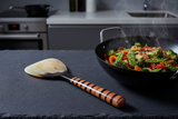 Haitian horn rice paddle beside wok with stir-fried vegetables on dark slate minimalist kitchen