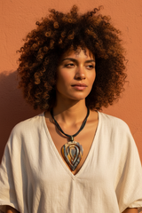 Haitian horn teardrop pendant necklace worn by woman with natural hair in cream linen top against terracotta wall