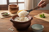Haitian horn rice paddle scooping jasmine rice from clay pot into bowl on rustic wooden surface