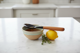 Haitian horn and wood spoon resting across honey bowl beside lemon and thyme on white marble counter