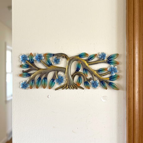 Tiny Haitian steel drum tree with blue flowers beside a wood-trimmed doorway