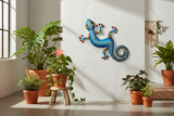Haitian hand-painted blue metal gecko wall art mounted on white plaster wall with tropical plants