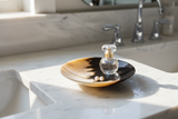 Haitian two-tone horn bowl holding gold necklace and pearl earrings on white marble vanity