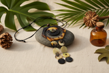 Haitian horn hexagon disc cascade necklace draped over dark stone beside tropical leaves and botanicals on linen