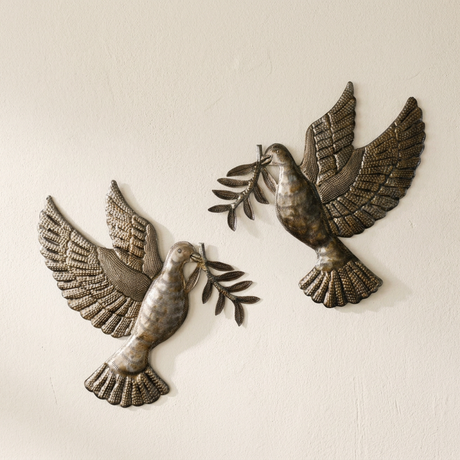 Close-up of two metal doves showing textured feathers, fan-shaped tails, and olive branches