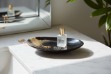 Haitian oval black horn dish holding gold necklace and diamond earrings on white marble vanity
