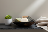 Haitian dark tortoiseshell horn bowl holding artisan soap bars on dark slate bathroom shelf