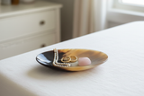 Haitian ivory horn dish holding pearl necklace and gold earrings on white linen dresser