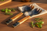 Haitian amber horn salad fork beside matching spoon on warm walnut surface with linen napkin and herbs