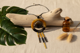 Haitian horn ring bar fringe necklace draped over driftwood beside tropical leaves and amber bottle on linen