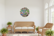 Colorful Haitian painted dragonfly round metal wall art mounted on a bright white sunroom wall with wicker furniture and potted ferns