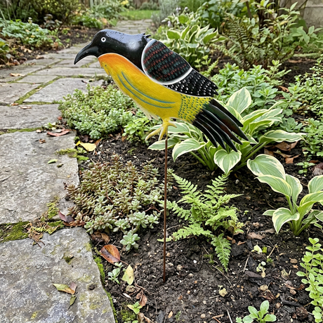 Yellow and black metal bird stake beside a stone garden path