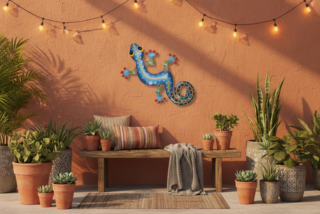 Haitian hand-painted blue metal gecko wall art on terracotta outdoor patio wall with string lights and succulents