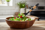 Haitian striped horn fork tossing fresh green salad in wooden bowl on farmhouse kitchen counter