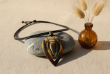 Haitian horn pendant necklace draped over river stone beside pampas grass and amber bottle on linen surface