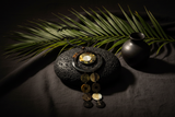 Haitian horn dark ring triple disc cascade necklace draped over black volcanic stone beside tropical leaves on dark linen