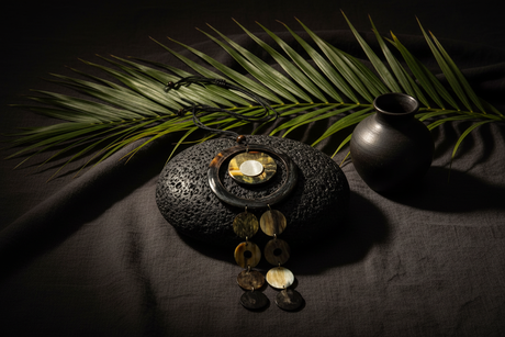 Haitian horn dark ring triple disc cascade necklace draped over black volcanic stone beside tropical leaves on dark linen