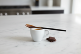 Haitian two-tone horn spoon across white espresso cup with dark chocolate on marble surface