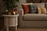 Haitian hand-painted metal lantern on a bohemian living room side table beside a linen sofa with throw pillows and warm candlelight