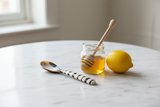 Haitian striped horn spoon beside honey jar and lemon on marble surface in morning light
