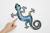 Haitian hand-painted metal gecko wall art shown next to a hand for scale, approximately 27 inches wide