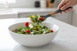 Haitian all-horn salad fork tossing arugula salad with tomatoes and parmesan in white ceramic bowl
